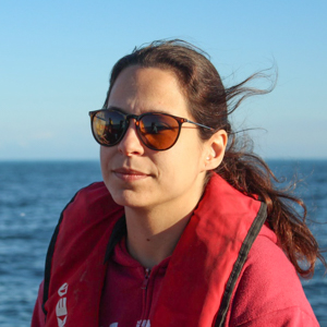 Woman wearing red life jacket and sunglasses with ocean in the background.