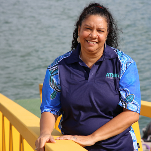 Woman with dark hair wearing blue shirt standing in front of yellow bridge.