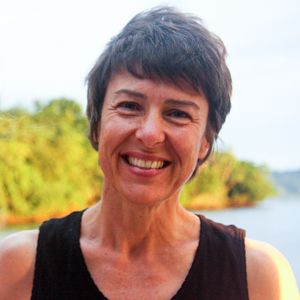 Woman with short dark hair wearing black singlet, standing in front of island and water