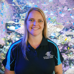 Woman with blonde hair wearing blue shirt, standing in front of colourful background.