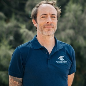 man wearing navy shirt and glasses stadning in front of green bushes