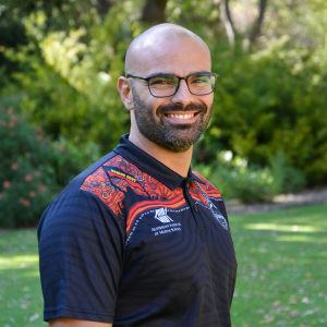 man wearing navy shirt and glasses stadning in front of green bushes