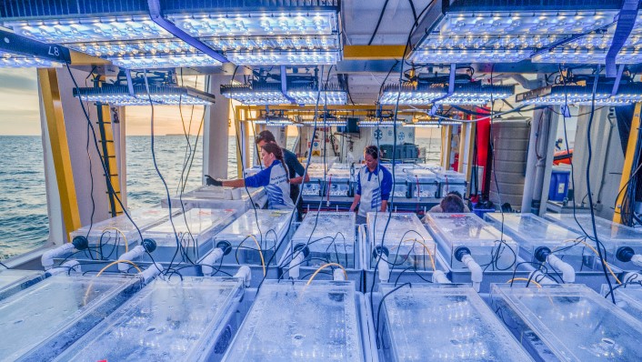 three people in AIMS sharits are working with many tanks on a big vessel while the sun sets