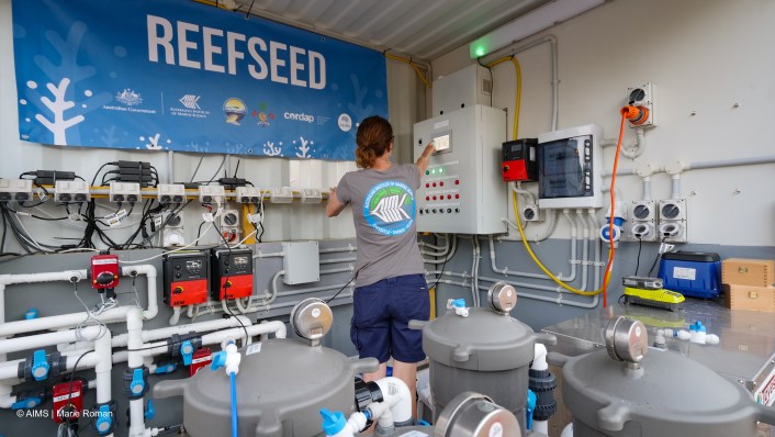 many pipes and controlled boards on a wall near large water tanks with a ReefSeed banner on the wall