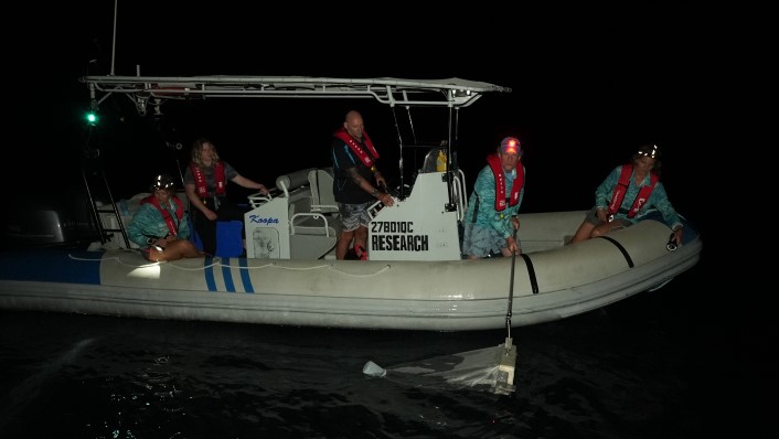 a small boat at night with people placing nets in the water