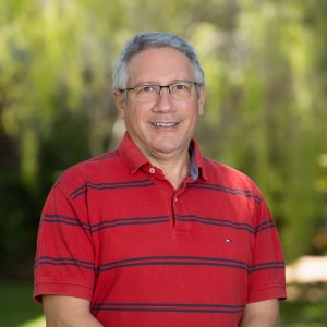 Man wearing red shirt standing in front of a leafy green background