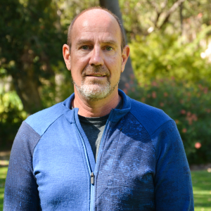 Man wearing blue jacket standing in front of green garden.