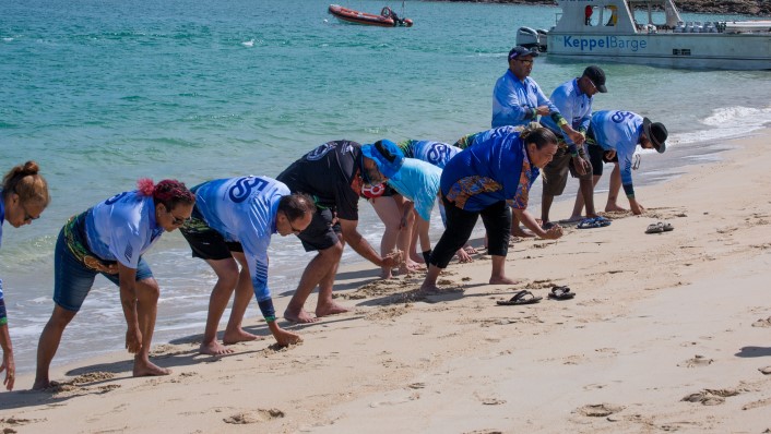 a line of people on a beach bending down to pick up sand