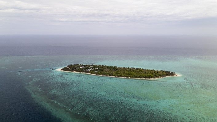 a small green island surrounded by white beaches and reef, as viewed from the air