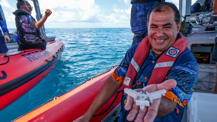 A man on a boat with his hand stretched out to the camera. on the palm of his hand is a white object with three points