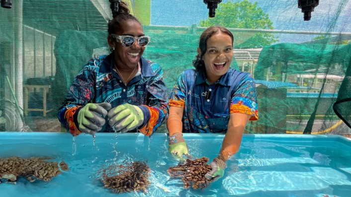 Two women laugh as they examine corals in a tank