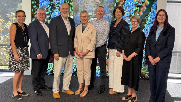 8 people standing in a grouped line, smiling at the camera in front of an AIMS logo