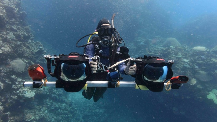 A person SUBA diving with a camera system in front of them, which has 2 cameras joined by a bar