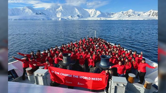 a large number of people on the bow of a large vessel with icebergs in the background