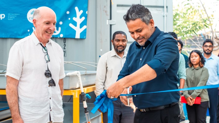 two people smiling as a group of people watch one of the people cut the ribbon