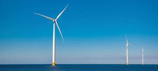 Three tall white windmills standing up out of an ocean scene with a clear sky