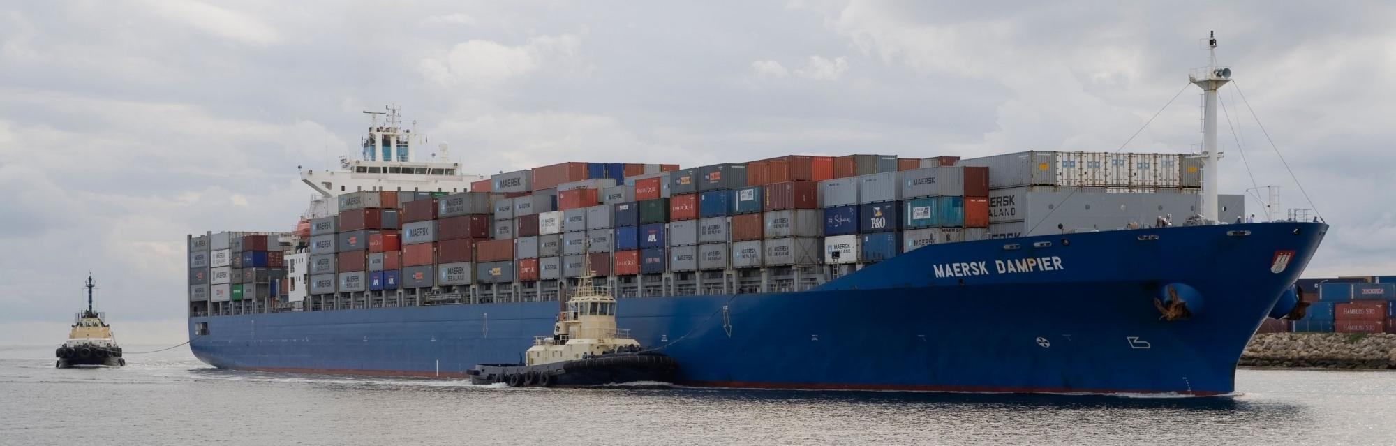 a cargo ship heads into port with two tug boats