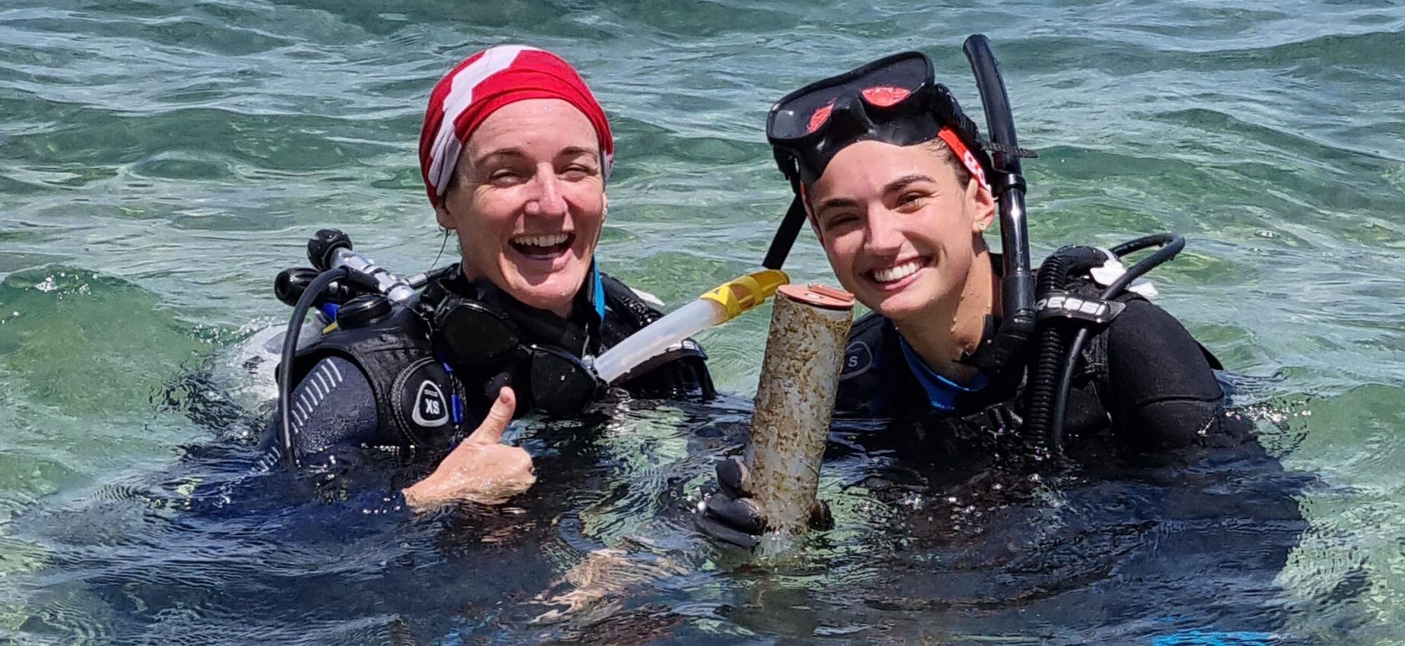 Two divers at the surface smiling and holding equipment that measure light