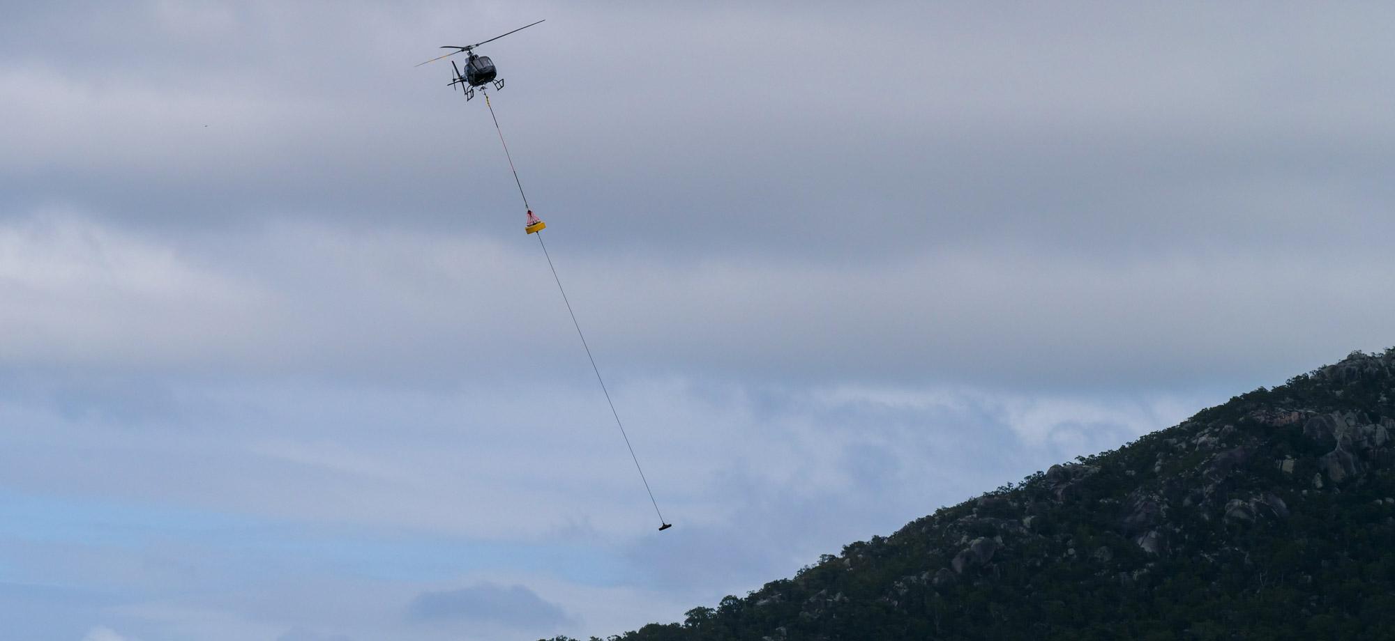 helicopter flies over a mountain with a cargo load hanging underneath