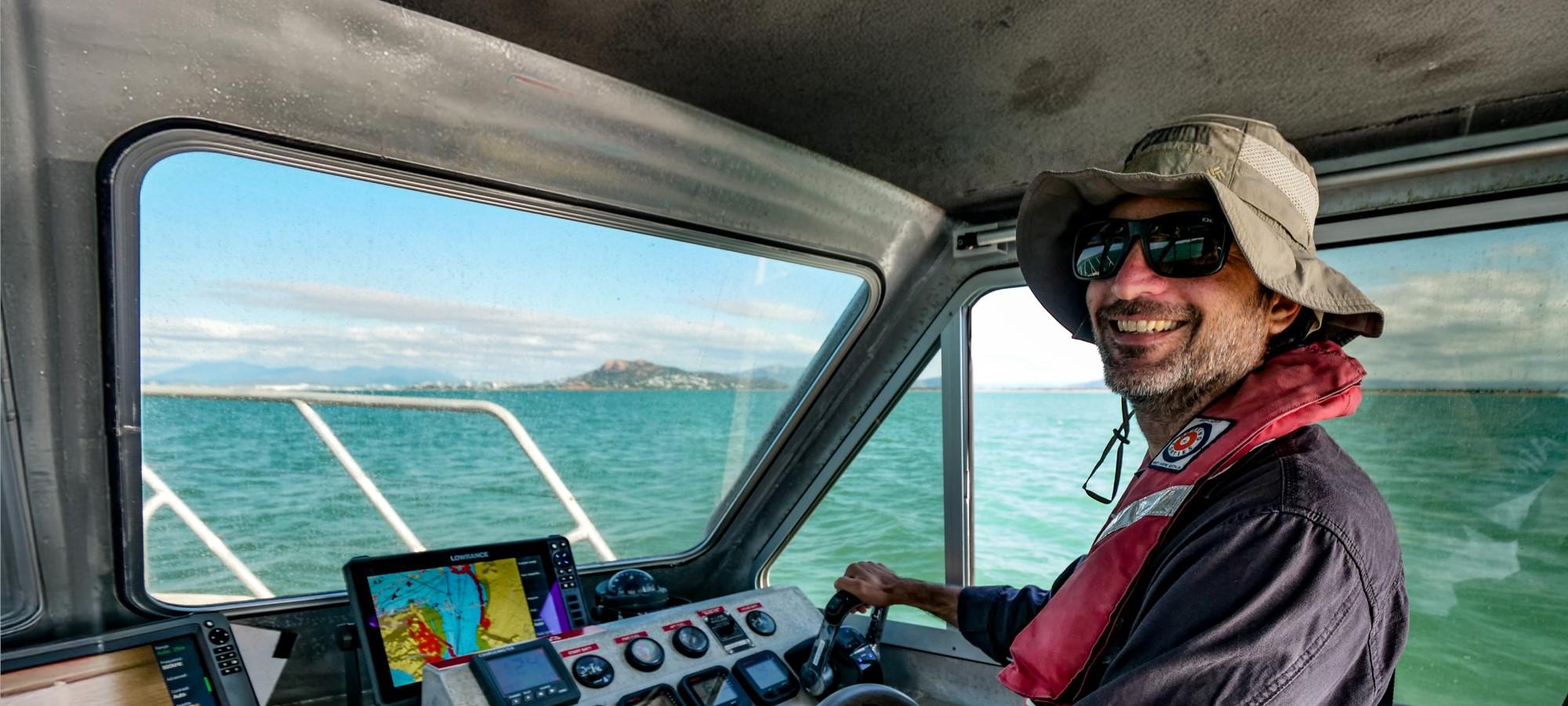 person driving small vessel from a cabin on a calm sea with land in the background