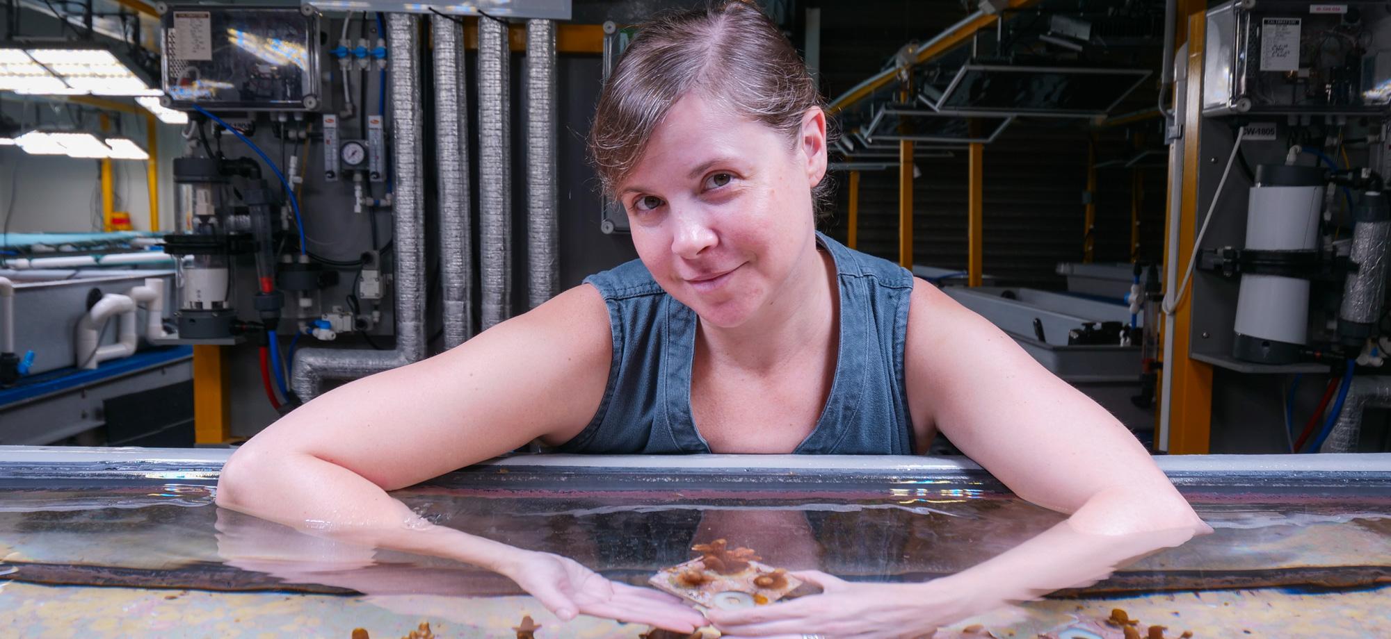 A woman is in an aquaria facility holding a small tray of coral fragments