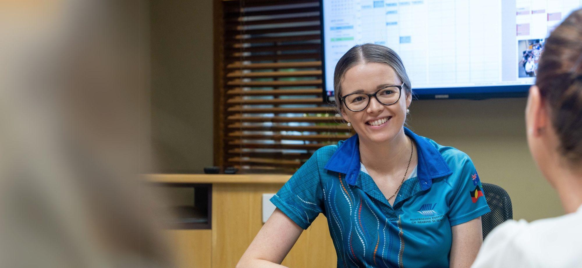 smiling woman in corporate style room looking at another person