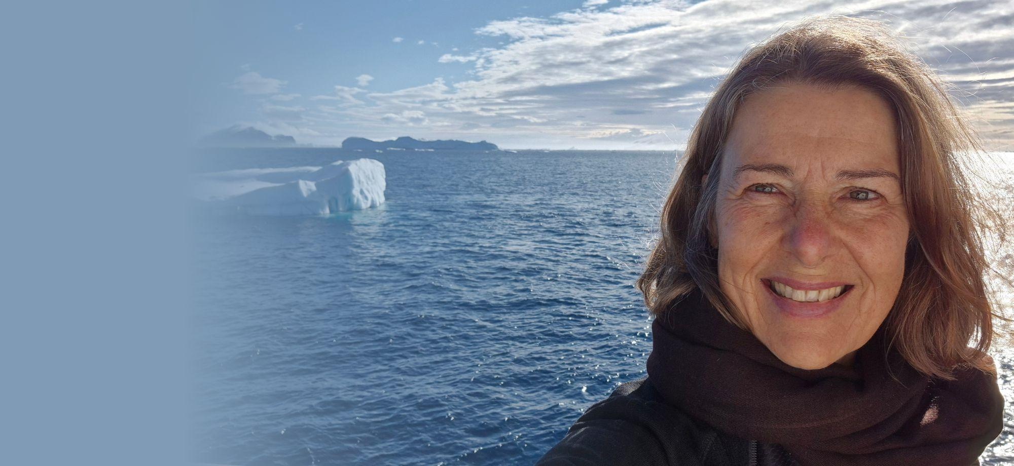 a woman smiling at the camera with the ocean and an icy landscape behind her