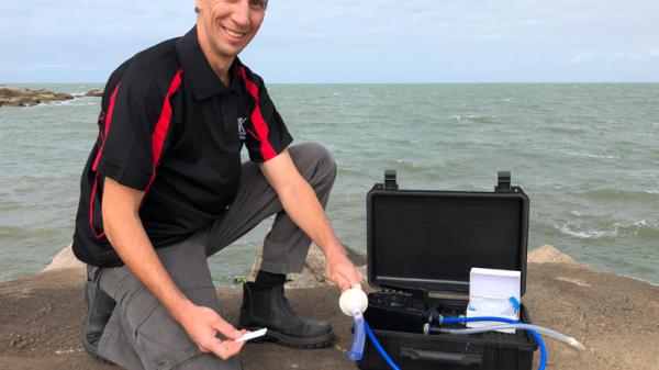 man kneeling next to box holding water sampling equipment and strip test.