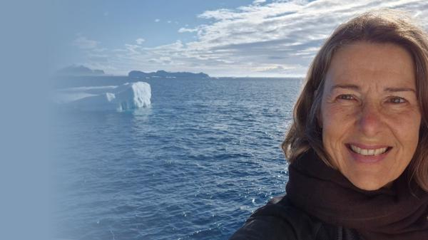 a woman smiling at the camera with the ocean and an icy landscape behind her