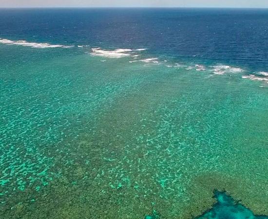 a birds eye view of a coral reef, with small waves breaking on the reef crest.