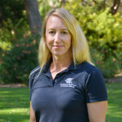 Woman wearing blue shirt, standing in front of green bushes