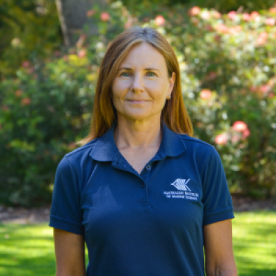 Woman wearing blue shirt, standing in front of green bushes