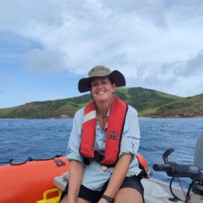 Woman in boat wearing blue shirt and green hat with an island in the background.