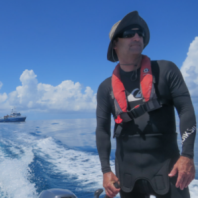 Man in wetsuit driving small boat.