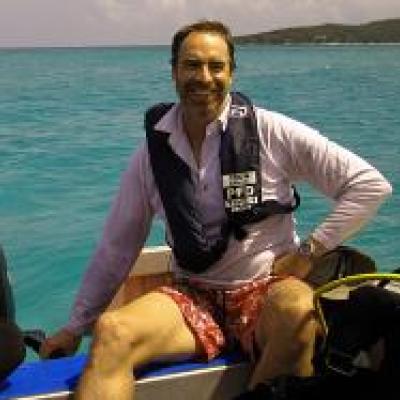 Man wearing life vest and long-sleeved shirt sitting in small boat with Ocean and Island in the background